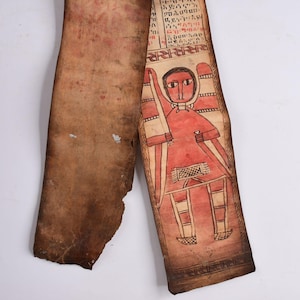 Puede incluir: Fragmento de manuscrito antiguo en pergamino. El fragmento presenta una ilustración roja y blanca de una figura sosteniendo una espada, con texto en un idioma desconocido. El pergamino es de color marrón con algo de desgaste.