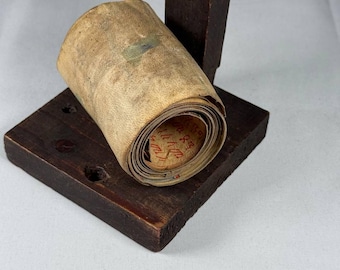 May include: A rolled up scroll of parchment paper with red writing on it, resting on a wooden stand.