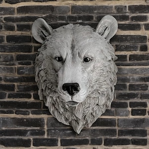 May include: A white, sculpted bear head mounted on a brick wall. The bear has a realistic fur texture and a detailed face.