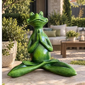 Op de afbeelding: Een groen kikkerbeeldje in een zittende meditatiehouding met gesloten ogen en de handen tegen elkaar in een gebedspositie. Het beeld heeft een gladde, glanzende afwerking met subtiele donkere schaduwen en een kalme uitdrukking.