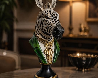 Puede incluir: Una escultura de busto de cebra con cabeza de rayas blancas y negras, chaqueta verde oscuro con detalles dorados en las solapas y corbatín dorado. La figura está montada sobre una base de pedestal negra con un anillo decorativo dorado.