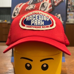 May include: A red and white baseball cap with a blue and white embroidered patch that says "Indianapolis Raceway Park Championship Racing".