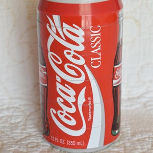 以下が含まれることがあります： 赤い白のコーラ缶のパズルで、「Coca-Cola Classic」と「Trademarks」の文字が側面に印刷されています。缶は12 fl oz（355 ml）です。