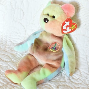 Könnte beinhalten: Ein Peace-Bär aus Plüsch im Tie-Dye-Look mit einem gestickten Peace-Zeichen auf der Brust. Der Bär hat ein rotes Ty-Herz-Etikett mit einem weißen Stern und den Worten "Beanie Babies" darauf.