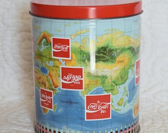 May include: A red and blue tin can with a world map design and Coca-Cola logos from different countries. The can has a red lid and a row of Coca-Cola bottles around the bottom.