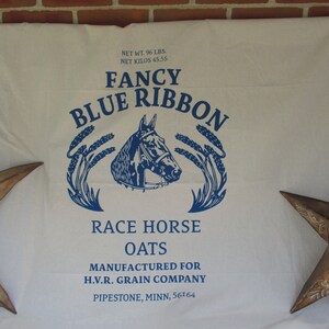 May include: A white fabric bag with blue text that reads "Fancy Blue Ribbon Race Horse Oats" and "Manufactured for H.V.R. Grain Company Pipestone, Minn. 56164". The bag features a blue illustration of a horse's head with wheat stalks on either side.