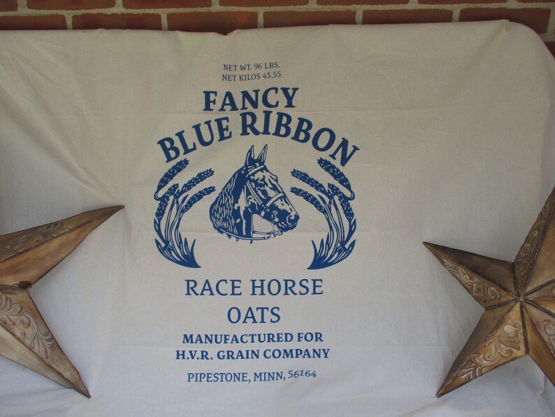 May include: A white fabric bag with blue text that reads "Fancy Blue Ribbon Race Horse Oats" and "Manufactured for H.V.R. Grain Company Pipestone, Minn. 56164". The bag features a blue illustration of a horse's head with wheat stalks on either side.