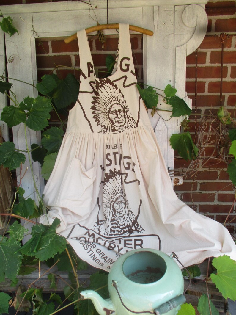 May include: A white cotton apron with a brown print of an American Indian chief and the text "Master By" and "100 LB. Bags Grain Postings".