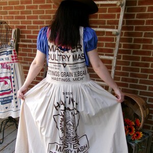 May include: A white cotton dress with a brown print of a vintage feed bag for "Master Poultry Mash" with the text "Hastings Grain & Bean Co. Hastings, Mich."