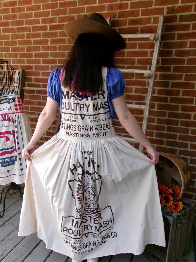 May include: A white cotton dress with a brown print of a vintage feed bag for "Master Poultry Mash" with the text "Hastings Grain & Bean Co. Hastings, Mich."