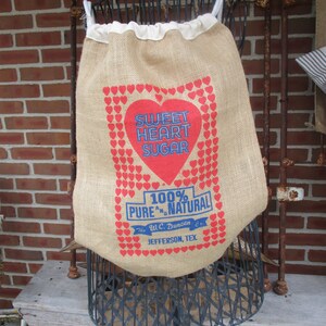 May include: A burlap sack with a red heart design that says "Sweet Heart Sugar 100% Pure & Natural The W.C. Duncan Co. Jefferson, Tex."