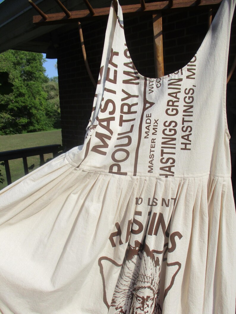 May include: A white cotton dress with a brown print of a Native American chief and the text "Hastings Grain" and "Master Mix Poultry Mash".