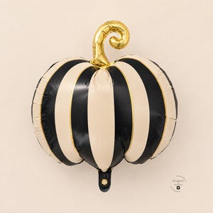 May include: A pumpkin-shaped foil balloon featuring alternating vertical stripes in black and cream colors. The balloon has a metallic gold stem at the top that curls to the right. A small logo with the text Designed by Moose is visible.