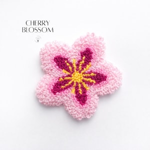 May include: A pink, five-petal flower with a textured, tufted appearance. The center of the flower is yellow, surrounded by a deep magenta. The text "CHERRY BLOSSOM" is in the upper left corner.