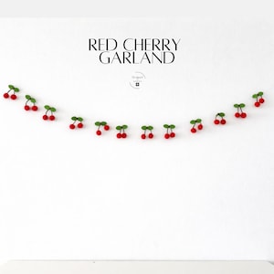 May include: A garland of red cherries with green leaves, strung together. The text "RED CHERRY GARLAND" is displayed above the garland in a black, elegant font. The garland is set against a white background.