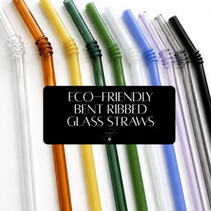 May include: A collection of bent, ribbed glass straws in various colors, including clear, amber, yellow, green, white, blue, purple, and black. The straws are arranged diagonally against a white background. Text on a black rectangle reads "ECO-FRIENDLY BENT RIBBED GLASS STRAWS."