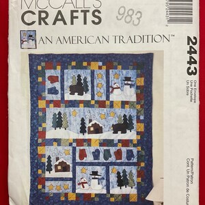 May include: A McCall's Crafts sewing pattern envelope 2443 featuring a quilt design with winter scenes. The quilt displays appliqued motifs of snowmen, bears, cabins, mittens, and yellow stars on a blue background with a patchwork border.