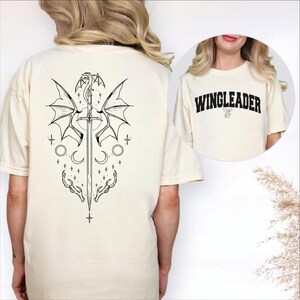 a white t-shirt with a graphic design on the back, including a dragon, a sword, and various celestial elements.