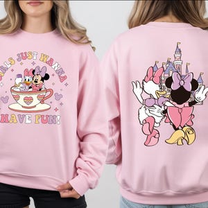 A woman wearing a pink sweatshirt with a cartoon image of Minnie Mouse and Donald Duck on it, along with the text "Girls just wanna have fun!" printed on the front.