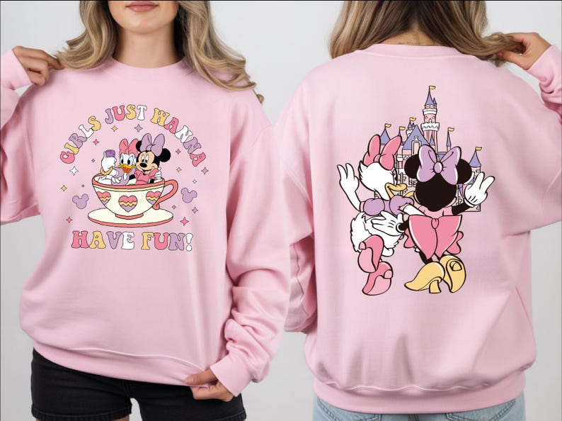 A woman wearing a pink sweatshirt with a cartoon image of Minnie Mouse and Donald Duck on it, along with the text "Girls just wanna have fun!" printed on the front.