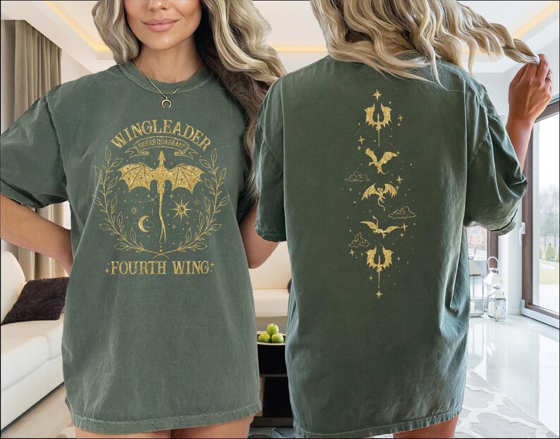 A woman wearing a green t-shirt with a dragon design and text on it, standing in a room with a window and a couch visible in the background.