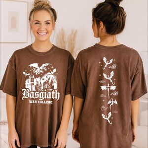 A woman wearing a brown t-shirt with a graphic design featuring a castle and dragons, smiling at the camera.