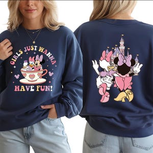 A woman wearing a navy blue sweatshirt with a graphic design featuring Minnie Mouse and Mickey Mouse in a cup, along with the text "Girls just wanna have fun!"
