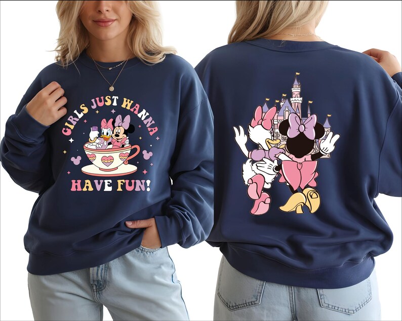 A woman wearing a navy blue sweatshirt with a graphic design featuring Minnie Mouse and Mickey Mouse in a cup, along with the text "Girls just wanna have fun!"