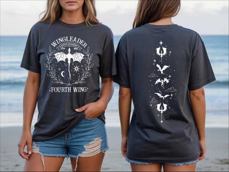 A woman wearing a black t-shirt with a graphic design featuring a bat and stars on the front and back, standing on a beach with the ocean in the background.