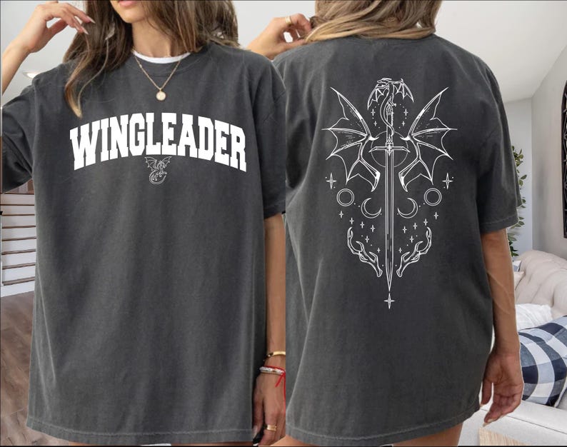 A woman wearing a grey t-shirt with the text "WINGLEADER" printed on it, along with a graphic design featuring a winged creature and a sword.