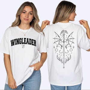 A woman wearing a white t-shirt with the text "WINGLEADER" printed on it, posing with her back to the camera.
