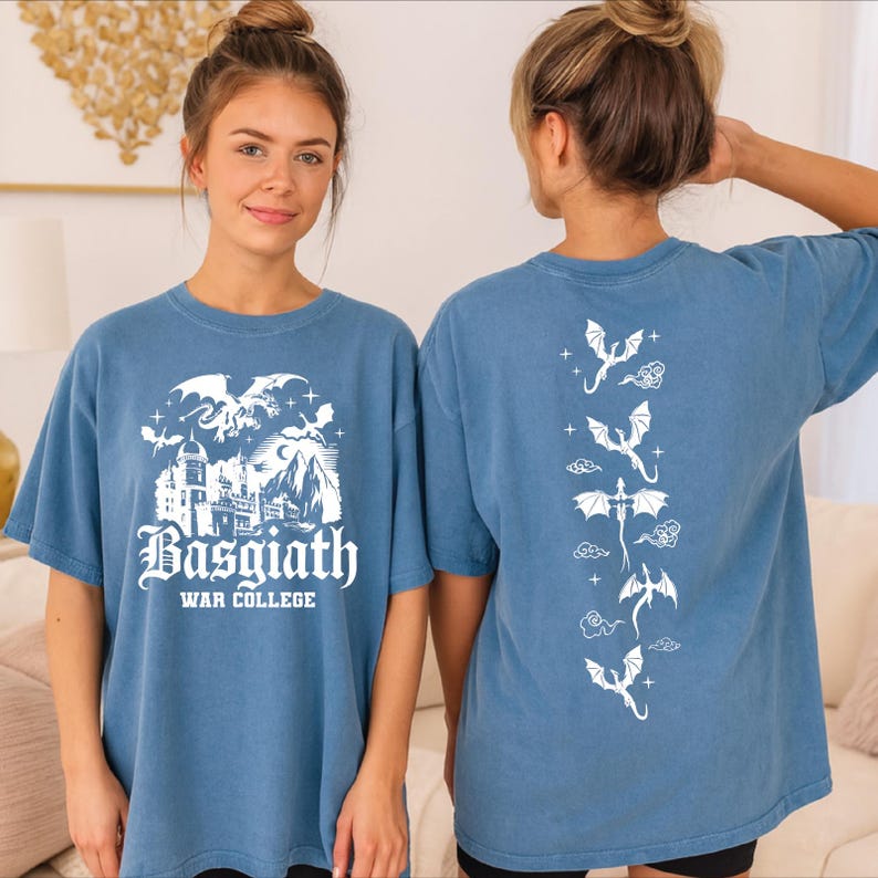 A woman wearing a blue t-shirt with a graphic design featuring a castle and dragons, standing in a room with a couch and a wall with a gold decoration.
