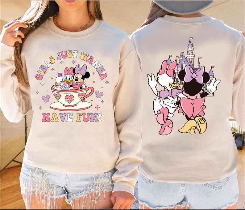 A woman wearing a white sweatshirt with a cartoon image of Minnie Mouse and Donald Duck on it, along with the text "Girls just wanna have fun!" printed on it.