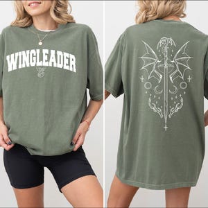 A woman wearing a green t-shirt with the text "WINGLEADER" printed on it, along with a graphic design featuring a dragon and stars.
