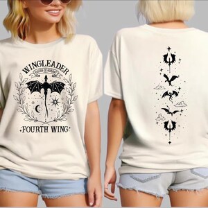 A woman wearing a white t-shirt with a graphic design featuring a dragon and the text "WINGLEADER - RIDER OF THE GARDEN - FOURTH WING".