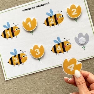 K&ouml;nnte beinhalten: Ein ausdruckbares Zahlen-Zuordnungs-Spiel zum Thema Bienen f&uuml;r Kinder. Das Spiel zeigt vier Bienen mit den Zahlen 1 bis 4 auf ihren K&ouml;rpern und vier gelbe Bl&uuml;tenformen mit den entsprechenden Zahlen. Das Spiel soll Kindern helfen, Zahlen zuzuordnen.