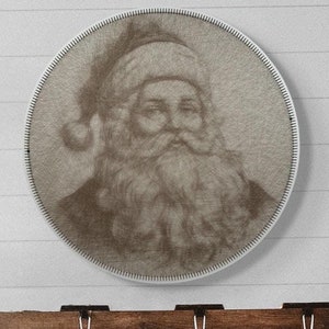 May include: A white wood wall with a round, white frame with a brown and white image of Santa Claus. Below the frame is a brown wooden shelf with three white stockings hanging from it.