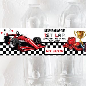 Op de afbeelding: Waterflesetiketten met een racewagenthema. De etiketten tonen een rode raceauto, een gouden trofee en de tekst "Brian's 1st Lap Around the Track, May 4, 20XX". De etiketten bevatten ook een geblokt vlagontwerp en de woorden "Pit Stop".
