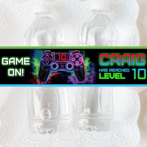 May include: Water bottle labels featuring a neon green, pink, and blue video game controller graphic. The text reads "Game On!" and "Craig has reached level 10".