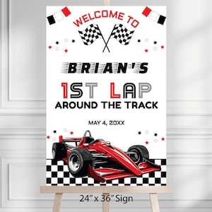 May include: A white sign with the text "WELCOME TO BRIAN'S 1ST LAP AROUND THE TRACK" in black and red. A red race car is at the bottom. The sign is 24" x 36".