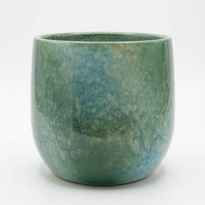 May include: A cylindrical ceramic cup featuring a mottled glaze in shades of seafoam green, forest green, and soft blue. The surface has a smooth, glossy finish with subtle, vein-like patterns throughout, creating a marbled appearance on the exterior.