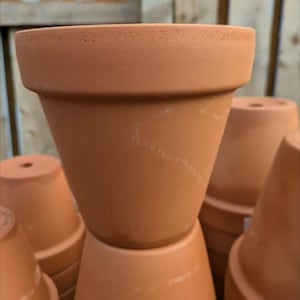 May include: Several terracotta plant pots stacked together. The pots have a traditional, conical shape with a broad rim. The unglazed clay has a slightly rough texture. These pots are suitable for planting flowers, herbs, or small plants.