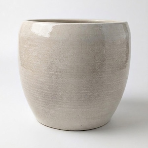 May include: A rounded ceramic planter with a glossy, light beige finish. The surface features subtle horizontal texture variations and a smooth, curved silhouette that tapers slightly towards the base, creating a simple, functional vessel for plants.