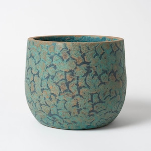 May include: A cylindrical ceramic planter featuring a textured, crackled surface finish in shades of teal, turquoise, and dark brown. The interior rim reveals a smooth, unglazed terracotta-coloured clay edge, contrasting with the exterior pattern.
