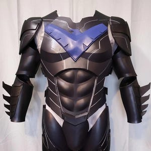 May include: A black and blue chest and arm armor set featuring a prominent blue bird emblem across the chest, sculpted abdominal plates, shoulder guards, and forearm gauntlets with three fin-like protrusions on each side of the outer arms.
