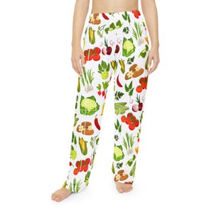 May include: White pajama pants with a colorful vegetable pattern. The design includes illustrations of tomatoes, onions, corn, cauliflower, and other vegetables. The pants are loose-fitting and made of a soft material.