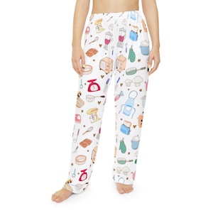 May include: White pajama trousers featuring a repeating pattern of baking-themed illustrations in various colours. The design includes mixers, blenders, measuring cups, and other kitchen tools. The trousers are loose-fitting and made of a soft material.