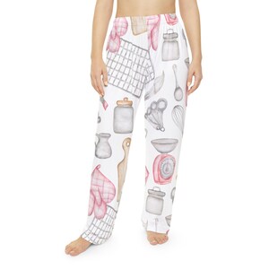 May include: White pajama pants with a watercolor pattern of kitchen tools and baking supplies. The design includes pink oven mitts, measuring spoons, jars, and a scale. The pants are loose-fitting and comfortable.