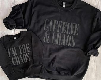 May include: Two black sweatshirts with matching text. The larger sweatshirt says "Caffeine & Chaos" and the smaller sweatshirt says "I'm the Chaos".