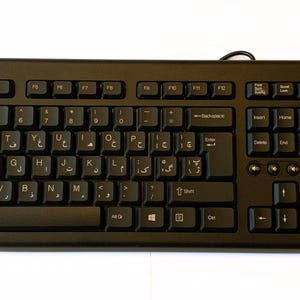 May include: A black computer keyboard featuring a standard QWERTY layout with additional Arabic script characters printed on the keys. The device includes a full numeric keypad, function keys, and a wired connection extending from the top edge.